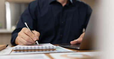person writing in notebook with laptop on table showcasing productivity and organization skills